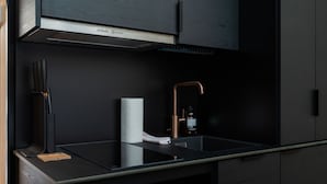 Una cocina moderna con encimera negra, campana extractora de acero inoxidable y grifo de cobre, además de una botella de jabón para manos.