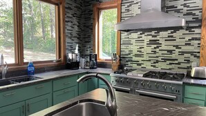 A modern kitchen with green cabinets, a stainless steel sink, and a gas stove.