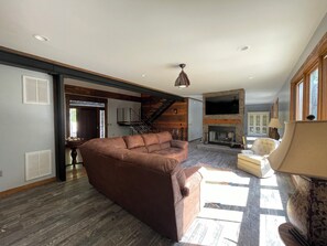 Ein geräumiges Wohnzimmer mit einem braunen Ecksofa, einem Kamin und einer Treppe, die zu einer oberen Ebene führt.
