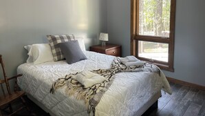 A bedroom with a large window, a bed with a quilt, pillows, a nightstand, and a chair.