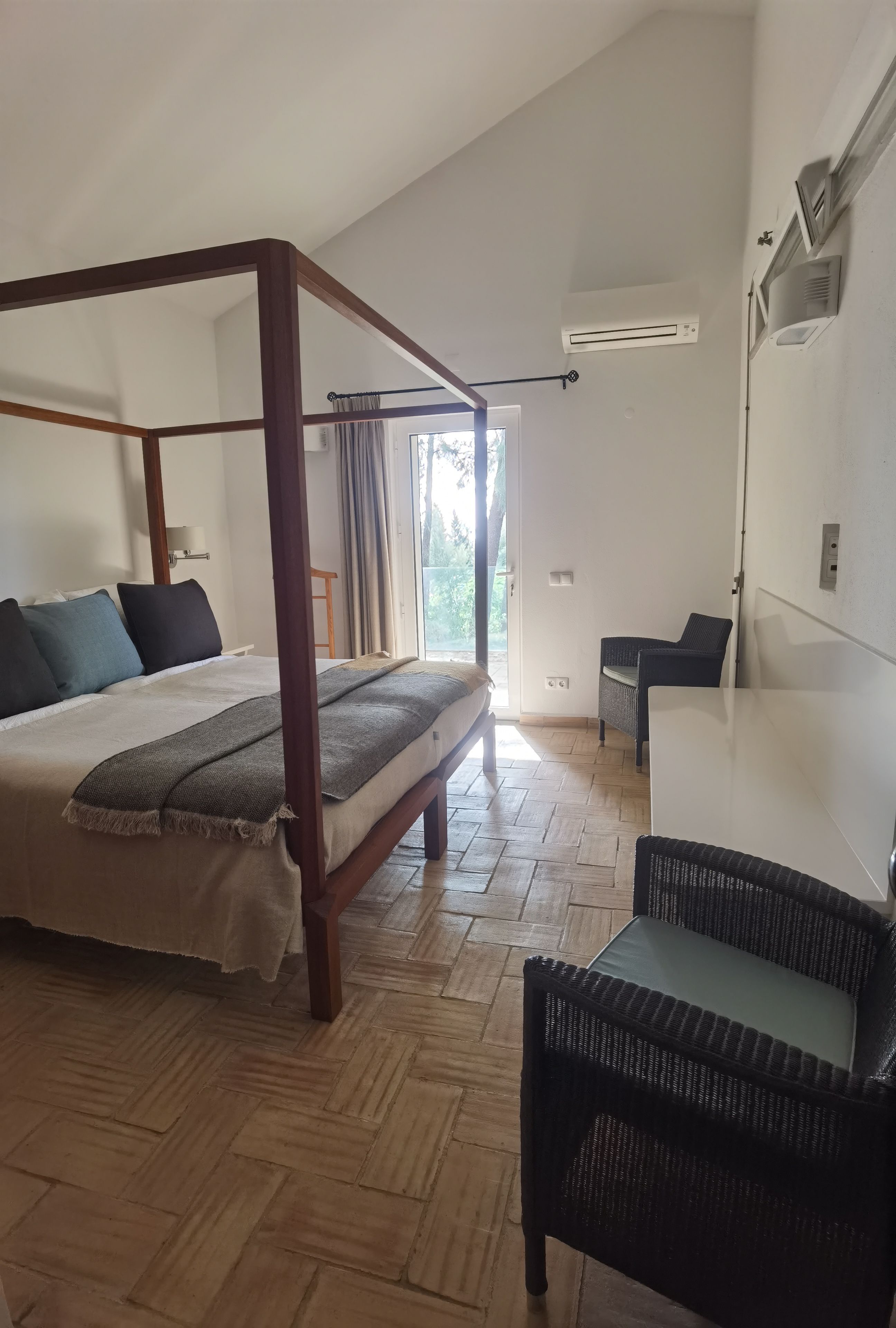 Une chambre à coucher avec un lit à baldaquin, une petite table, une chaise et une grande fenêtre avec des rideaux.