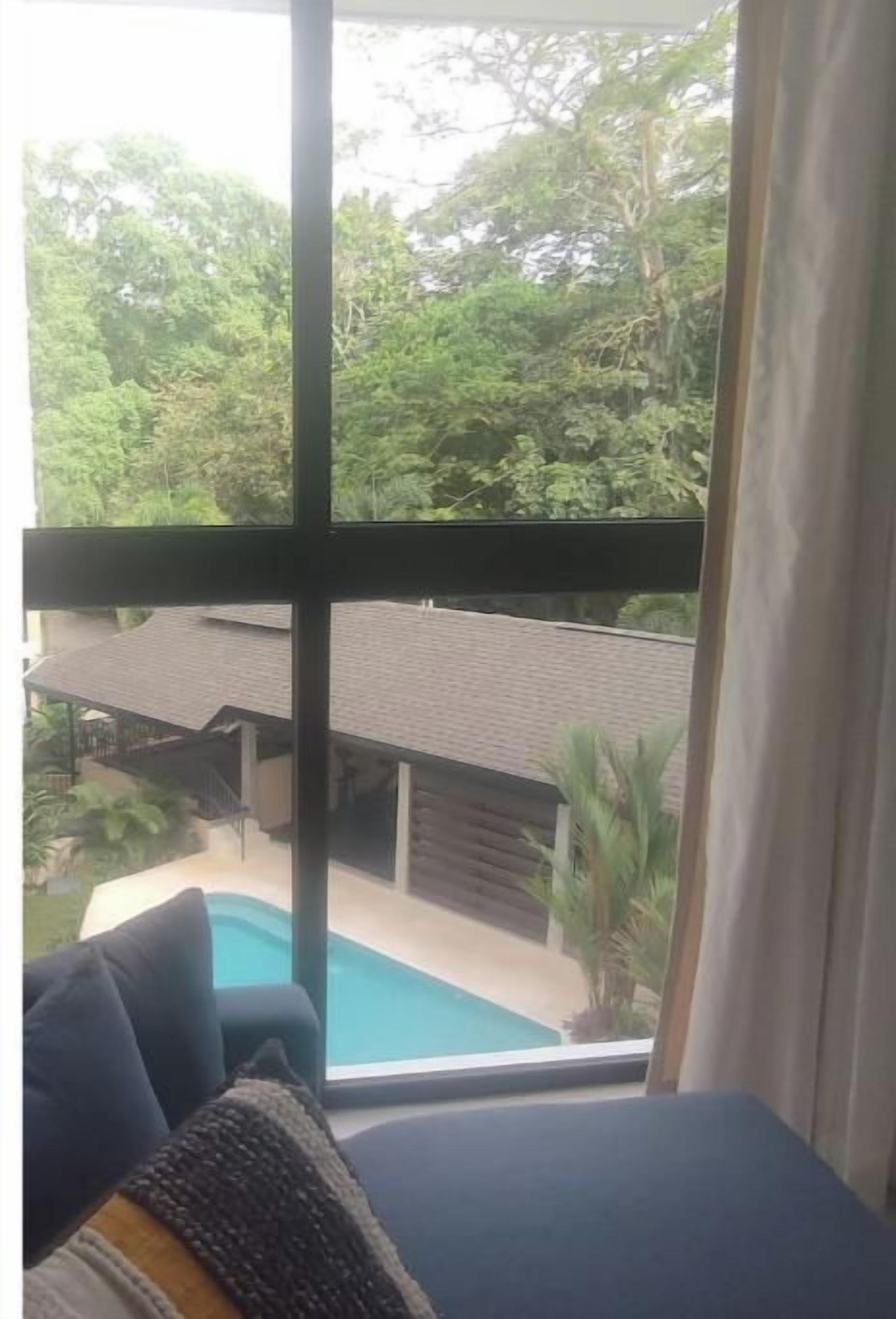 A room with a large window overlooking a swimming pool and lush greenery.