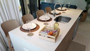 A modern kitchen with a central island, a sink, and a dining area with chairs and plates. - Stylish 2 bed condo with mountain & pool view (Jaco)