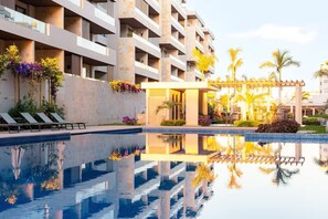 A modern hotel with a swimming pool, lounge chairs, and a covered outdoor area with plants.