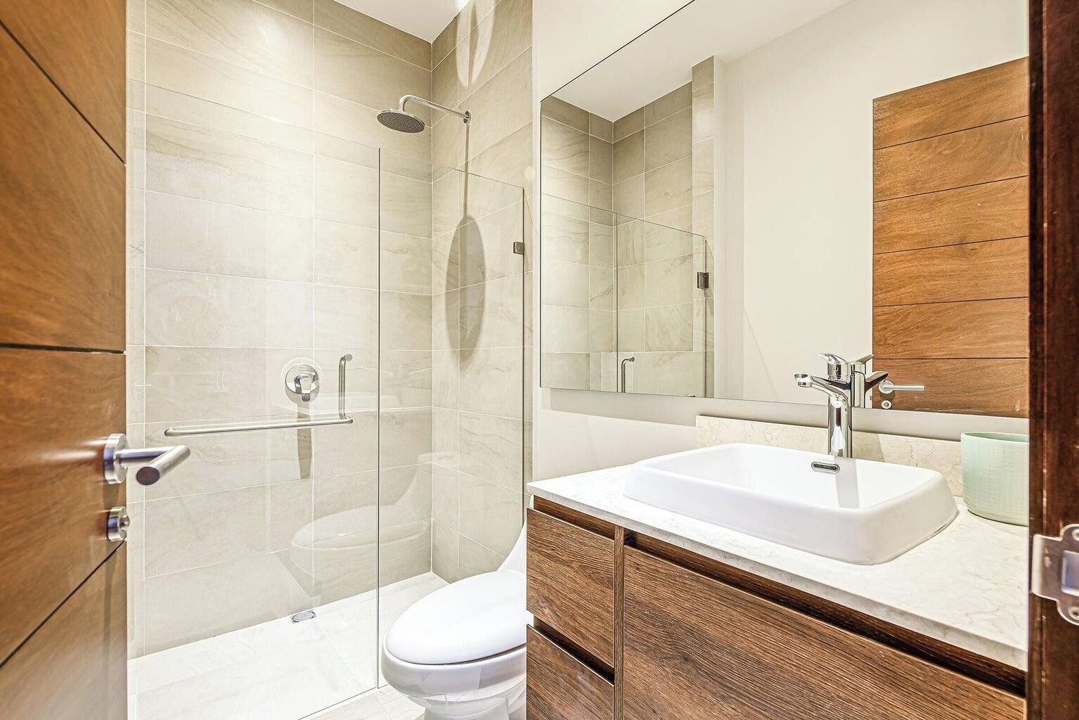 Ein modernes Badezimmer mit einer Duschkabine aus Glas, einer weißen Toilette und einem großen Waschbecken mit Holzschrank.