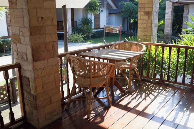 A wooden deck with a table and chairs, a stone pillar, and a view of a house and greenery.