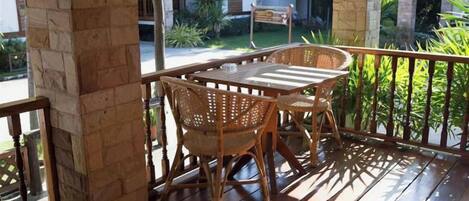 A wooden deck with a table and chairs, a stone pillar, and a view of a house and greenery.