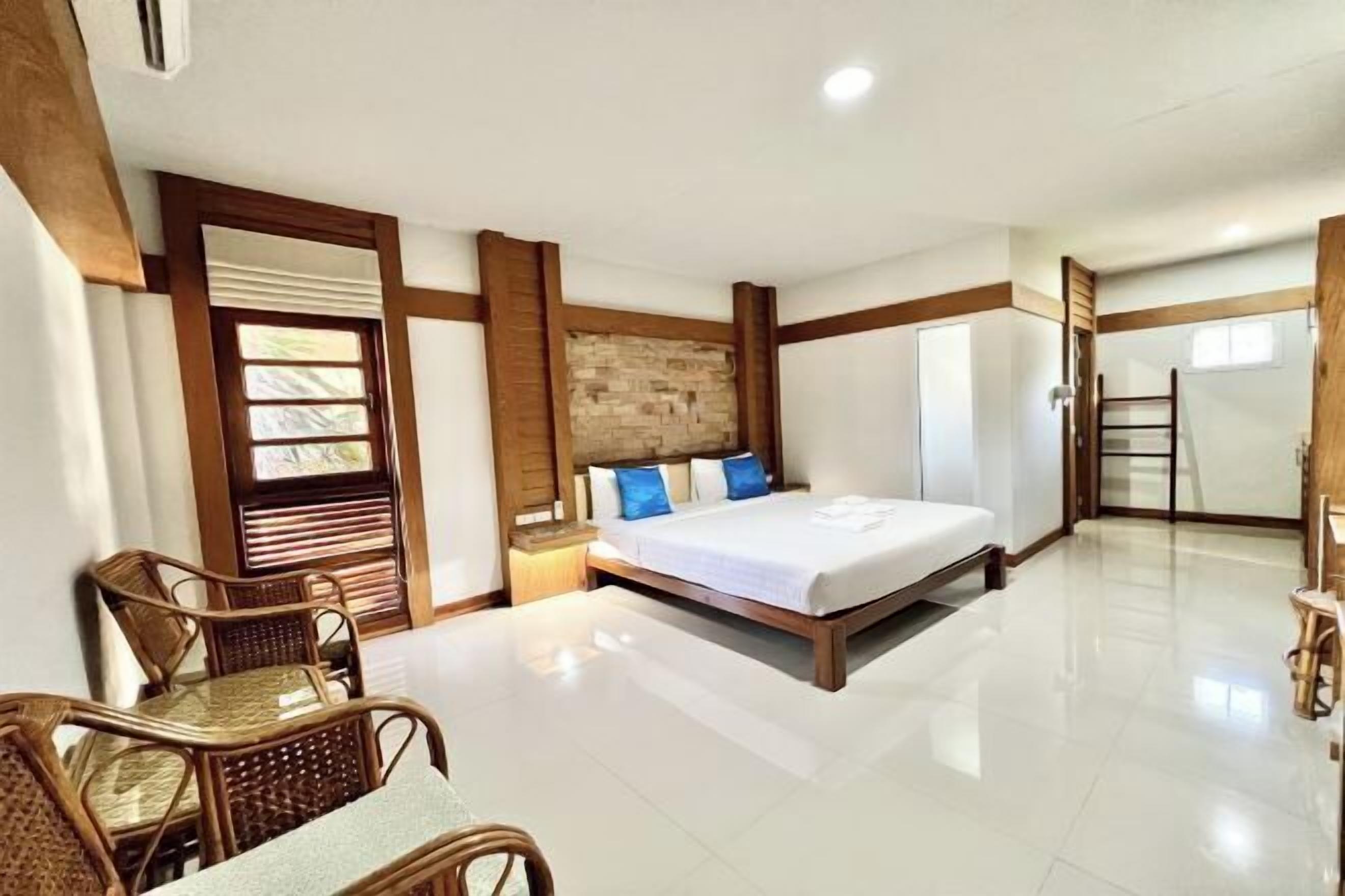 A hotel room with a bed, a wooden headboard, a nightstand, a wicker chair, and a view of the outside.