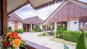 A covered outdoor area with a concrete floor, surrounded by buildings with wooden roofs and walls. There are potted plants and a bench visible. - Ruentara Resort & Villa (Buri Ram)