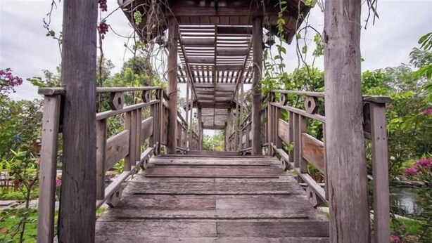 A wooden staircase leading up to a covered area with railings, surrounded by greenery. - Ruentara Resort & Villa (Buri Ram)