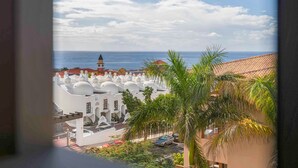 A coastal view with white buildings, a palm tree, and a distant tower. - Holiday Apartment 'Palm Serenity' with Shared Pool, Wi-Fi and Air Conditioning (Santa Cruz de Tenerife)