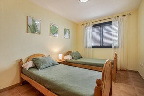 Een kamer met twee houten bedden, een raam met zonwering en een wandlamp.