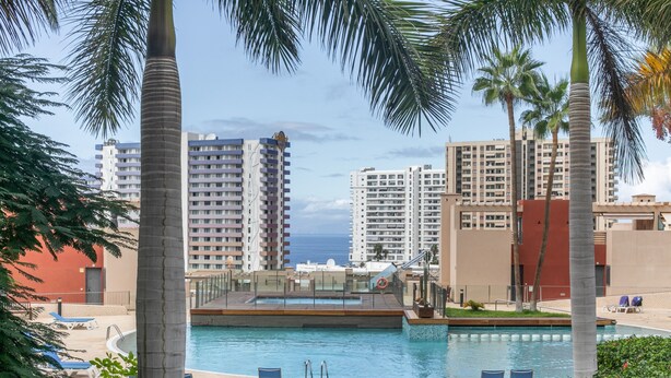 A pool area with lounge chairs, palm trees, and high-rise buildings in the background. - Holiday Apartment 'Palm Serenity' with Shared Pool, Wi-Fi and Air Conditioning (Santa Cruz de Tenerife)
