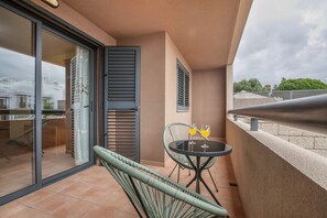 Een balkon met een glazen deur, een tafel met twee glazen sinaasappelsap en een rieten stoel.