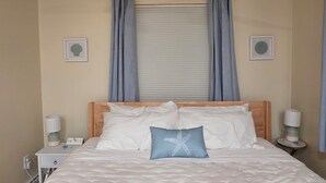 A bedroom with a bed, curtains, a window with blinds, bedside lamps, and wall art.