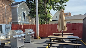 A parking lot with a barbecue grill, a picnic table, and a red picket fence.