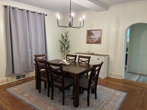 A dining area with a wooden table, six chairs, a chandelier, a potted plant, a painting, and a cabinet.