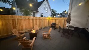 Patio sul retro con sedie di legno, un tavolo e un braciere.