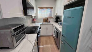 A compact kitchen with white cabinets, a built-in oven, a microwave, a sink, and a teal refrigerator.