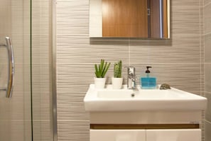 A bathroom with a white sink, two potted plants, a soap dispenser, and a mirror above the sink.