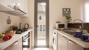 Cocina compacta con lavadora, microondas y pileta. Se ve una ventana con vista a edificios.