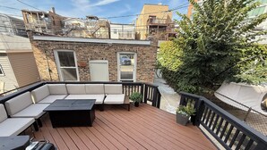 A deck with a black grill, a sofa, and a potted plant.