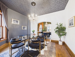 Uma sala de jantar com uma mesa de vidro, cadeiras pretas, um candelabro e um vaso com planta.