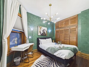 Quarto com cama, escrivaninha, cadeira e janela com cortinas.