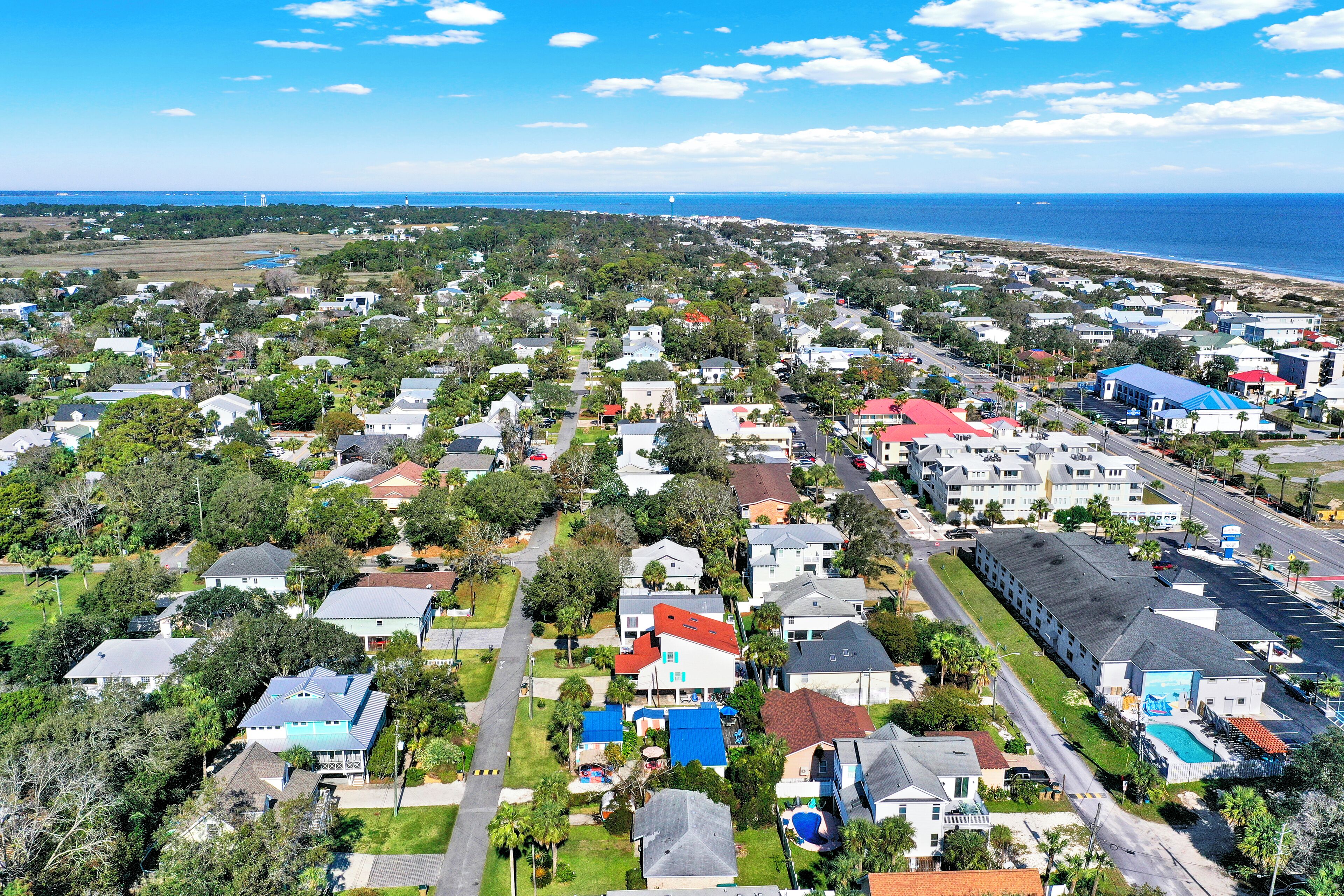 An aerial view of a residential area with houses, roads, and a beach in the background.