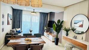 Una sala de estar moderna con comedor, ventanas grandes con cortinas, un televisor de pantalla plana y un espejo redondo en la pared.