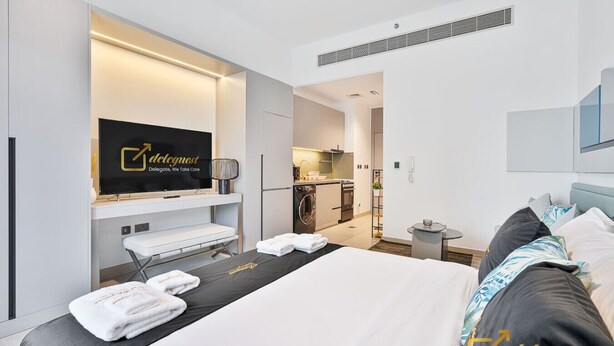 A modern hotel room with a bed, a TV, a small kitchenette, and a bathroom. - Posh Studio in MBR by Deleguest (Dubai)