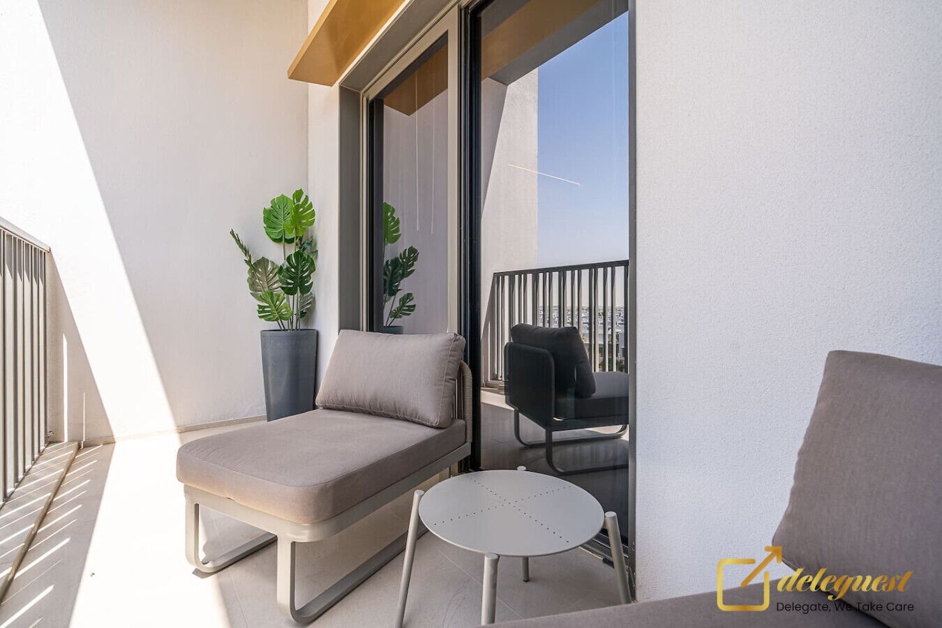 A balcony with a sofa, a small table, and two chairs. There are potted plants and a view of the city.