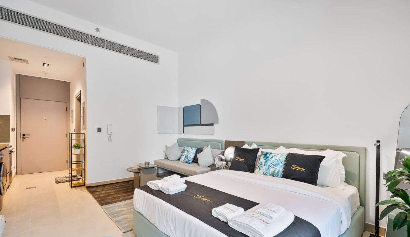 A modern hotel room with a large bed, a bedside table, a mirror, and a plant.