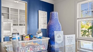 Habitación con pared azul, un jarrón decorativo grande, dispensador de agua, recipientes para snacks y un cartel que indica prohibido fumar.