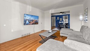 Una sala de estar moderna con piso de madera, un sofá gris, una mesa de centro y un televisor montado en la pared.