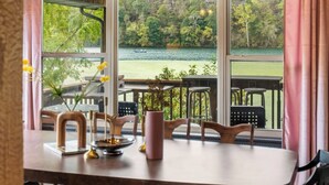 Een eetruimte met een tafel, stoelen en uitzicht op een meer en bos door grote ramen.