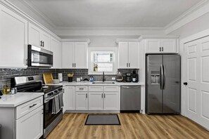 A modern kitchen with white cabinetry, stainless steel appliances, and a wooden floor.