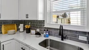 Een moderne keuken met witte kastjes, een roestvrijstalen spoelbak en een raam met zonwering.