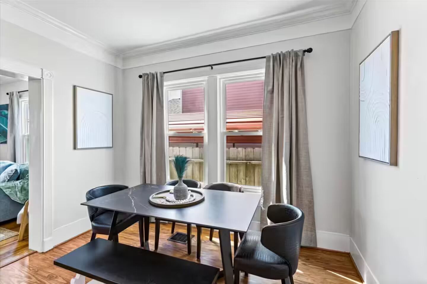 A dining area with a table and chairs, a view of the outside, and a window with curtains.