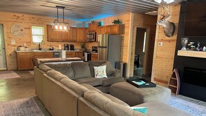 A spacious living area with a large sectional sofa, a kitchen with wooden cabinets, and a mounted deer head. - Cozy Cabin with hot tub, just minutes from Nolin lake and Mammoth Cave park! (Leitchfield)