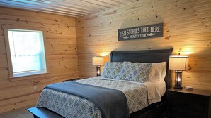 A wooden-paneled bedroom with a bed, two bedside lamps, a bench, and a sign above the bed. - Cozy Cabin with hot tub, just minutes from Nolin lake and Mammoth Cave park! (Leitchfield)