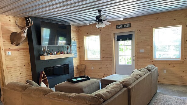 A cozy cabin interior with a large wooden sofa, a fireplace, a television, and a sign reading "LAKE HOUSE". - Cozy Cabin with hot tub, just minutes from Nolin lake and Mammoth Cave park! (Leitchfield)