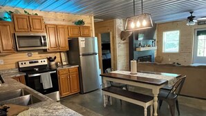 A kitchen with wooden cabinets, stainless steel appliances, a granite countertop, and a dining area with a bench. - Cozy Cabin with hot tub, just minutes from Nolin lake and Mammoth Cave park! (Leitchfield)