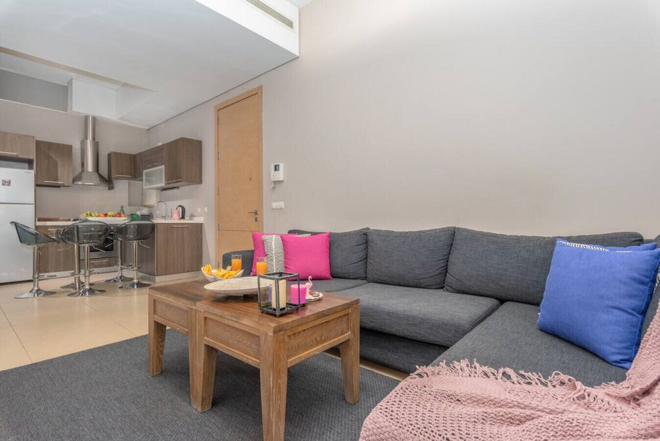 Un salon moderne avec un canapé gris, une table basse en bois et une cuisine en arrière-plan.