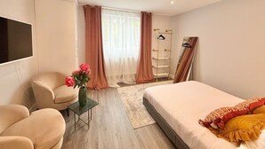 Una camera d'albergo moderna con un letto, un angolo salotto con poltrone, una televisione e una finestra con tende.