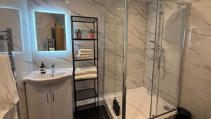 Un bagno moderno con parete in marmo, box doccia in vetro, ripiano in metallo nero con asciugamani e lavabo bianco.