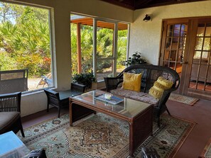 Une pièce avec une table basse en verre, un canapé en osier et une vue sur un jardin, grâce à de grandes fenêtres.