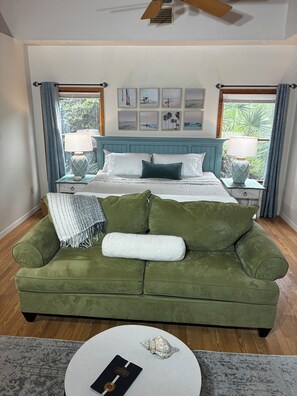 Une chambre à coucher avec un lit, un canapé vert, deux tables de chevet avec des lampes, un ventilateur de plafond et une fenêtre avec des rideaux.