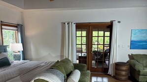A bedroom with a bed, a green sofa, a round coffee table, and a view through a glass door to an outdoor area.