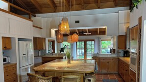 A spacious kitchen with wooden cabinets, a central island with chairs, a hanging light fixture, and a view to the outside.